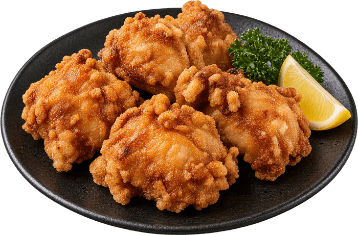 Des morceaux de poulet karaage dorés sur une assiette noire, avec un quartier de citron et du persil