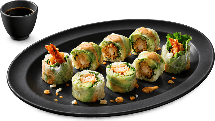 Des spring rolls enroulés dans une feuille de riz, sur une assiette noire, avec un bol de sauce soja